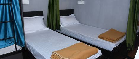 Two single beds with white linens, a green curtain, and a blue curtain.