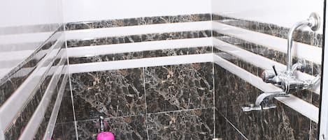 Un baño con piso de mármol, ducha con grifo de cromo y dos cubetas azules.