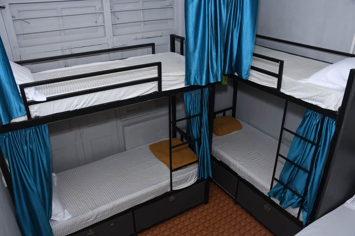 Une chambre avec des lits superposés, des rideaux bleus, du linge de lit blanc et un sol à motifs.
