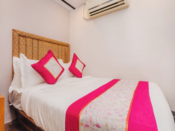 A neatly made bed with white and pink bedding, a wooden headboard, and a floral-patterned throw. - AFRA DORMITORY (Mumbai)