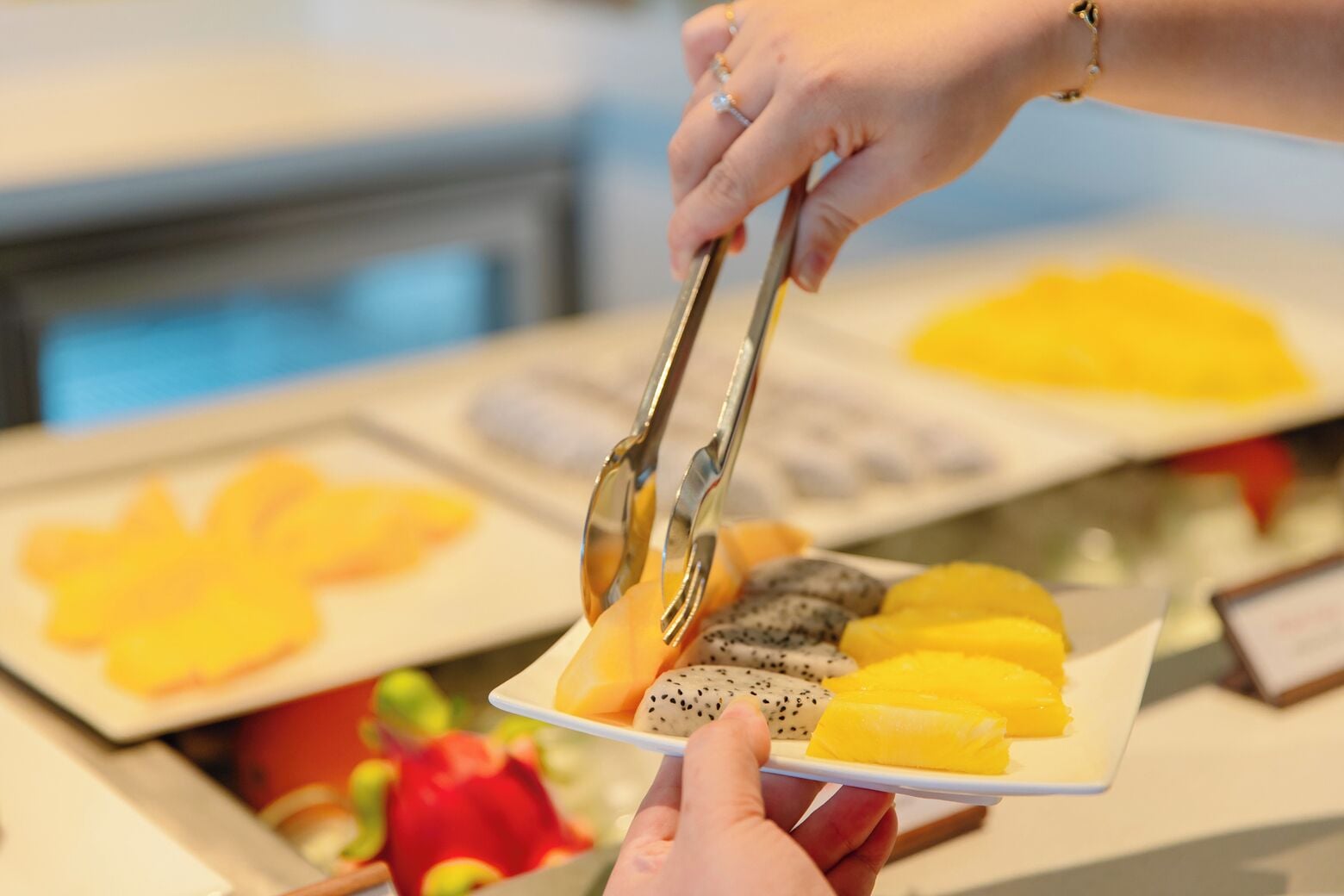 A person using tongs to serve fruit onto a plate.