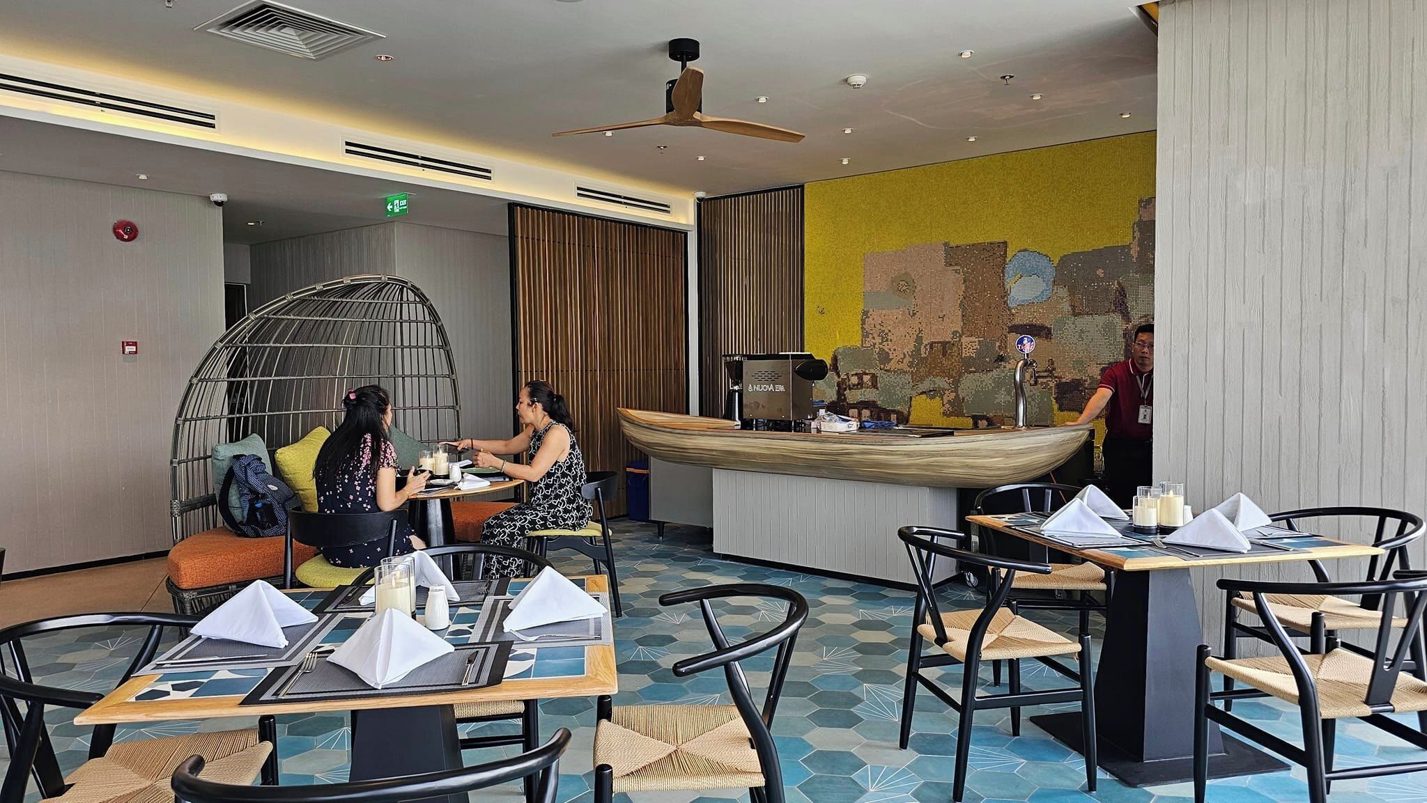 A restaurant with round tables, a high ceiling, and a mural on the wall.