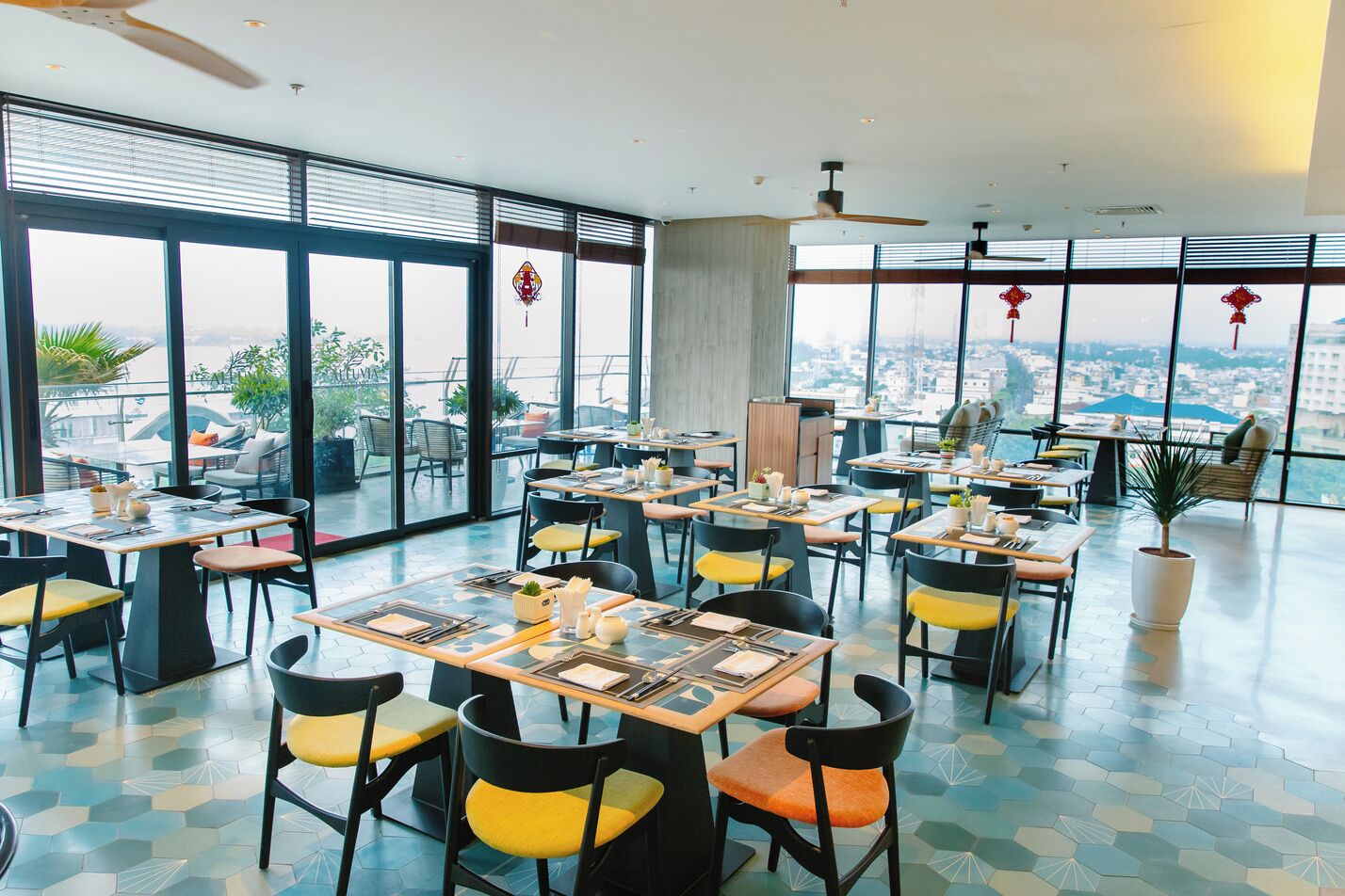 Un restaurant moderne doté de grandes fenêtres, de nombreuses tables et de chaises avec des coussins jaunes.