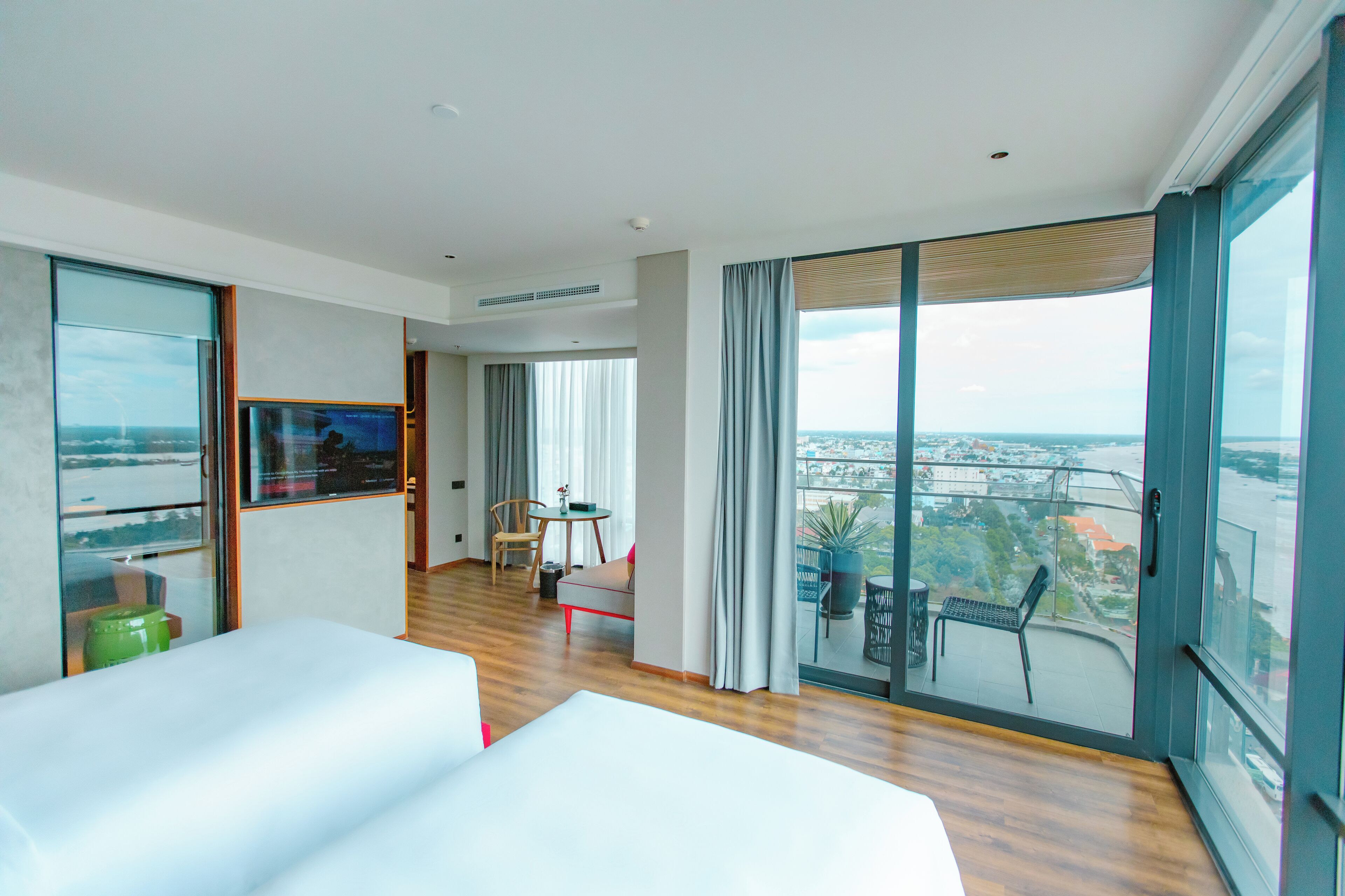 Ein modernes Hotelzimmer mit großem Balkon, Fernseher, Essbereich und Blick auf die Stadt.