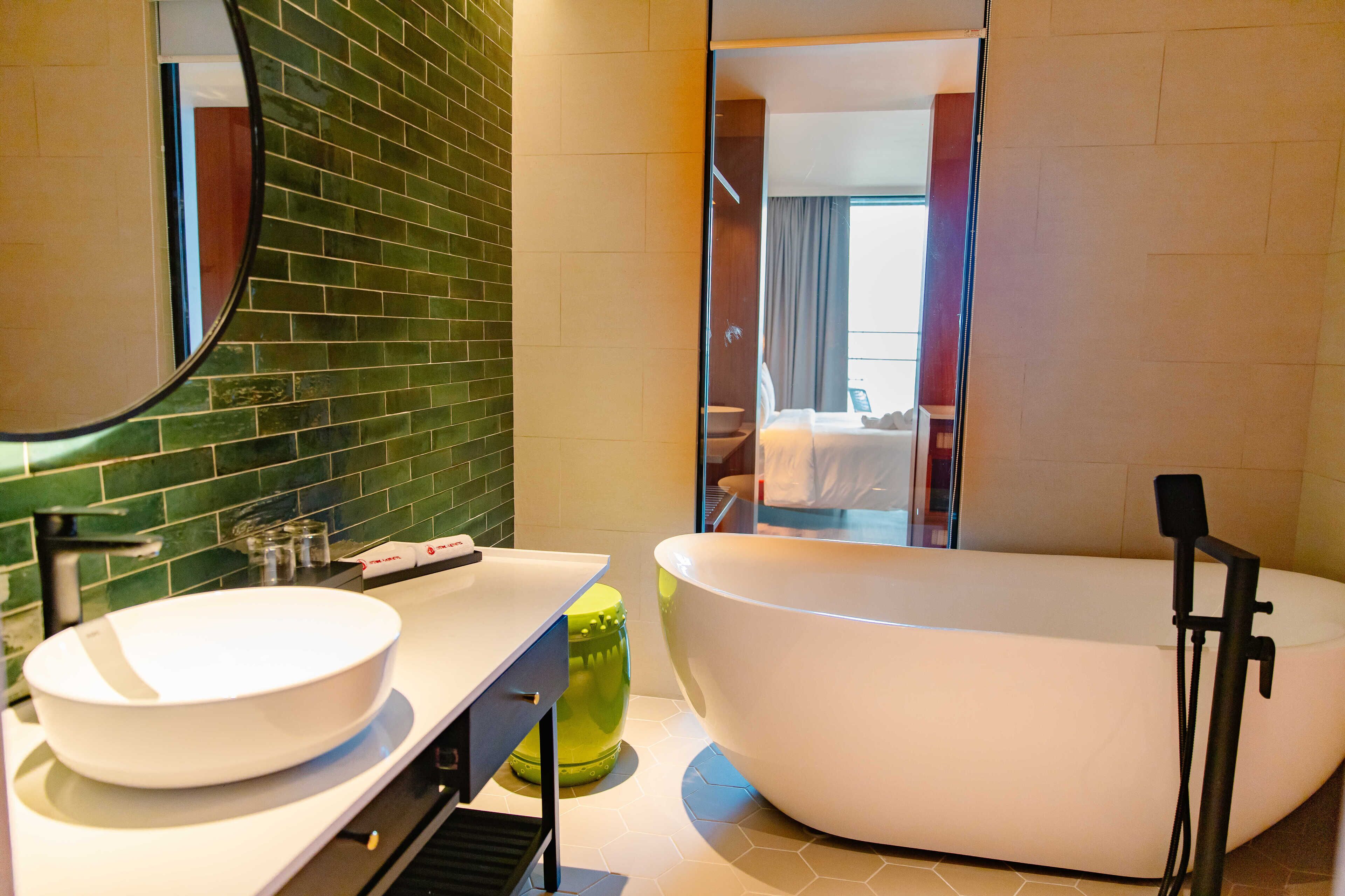 A modern bathroom with a freestanding bathtub, a large mirror, and a green-tiled backsplash.
