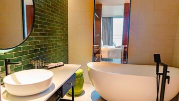 A modern bathroom with a freestanding bathtub, a large mirror, and a green-tiled backsplash.