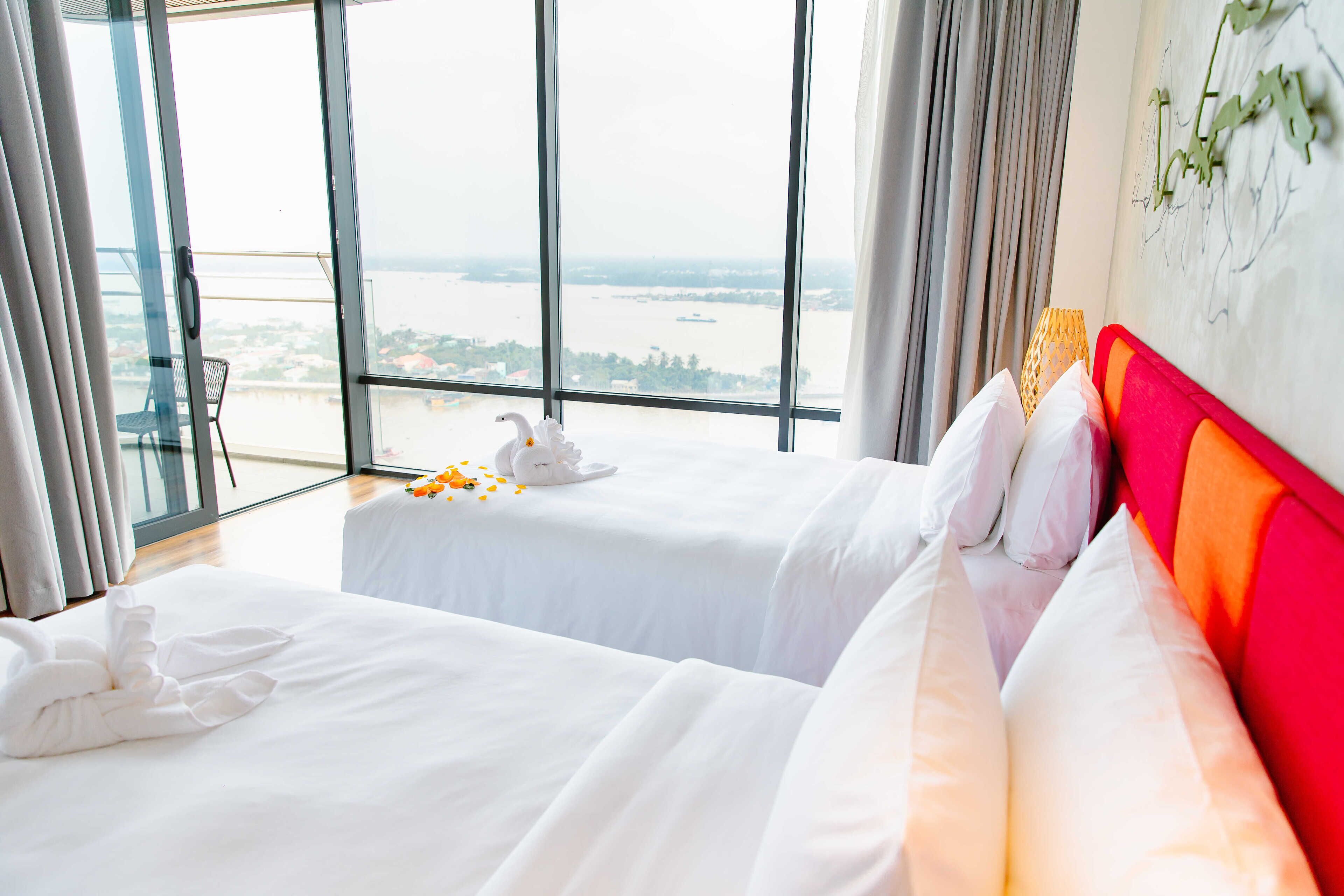 A hotel room with two beds, a large window with a view of a body of water, and a decorative swan on the window sill.