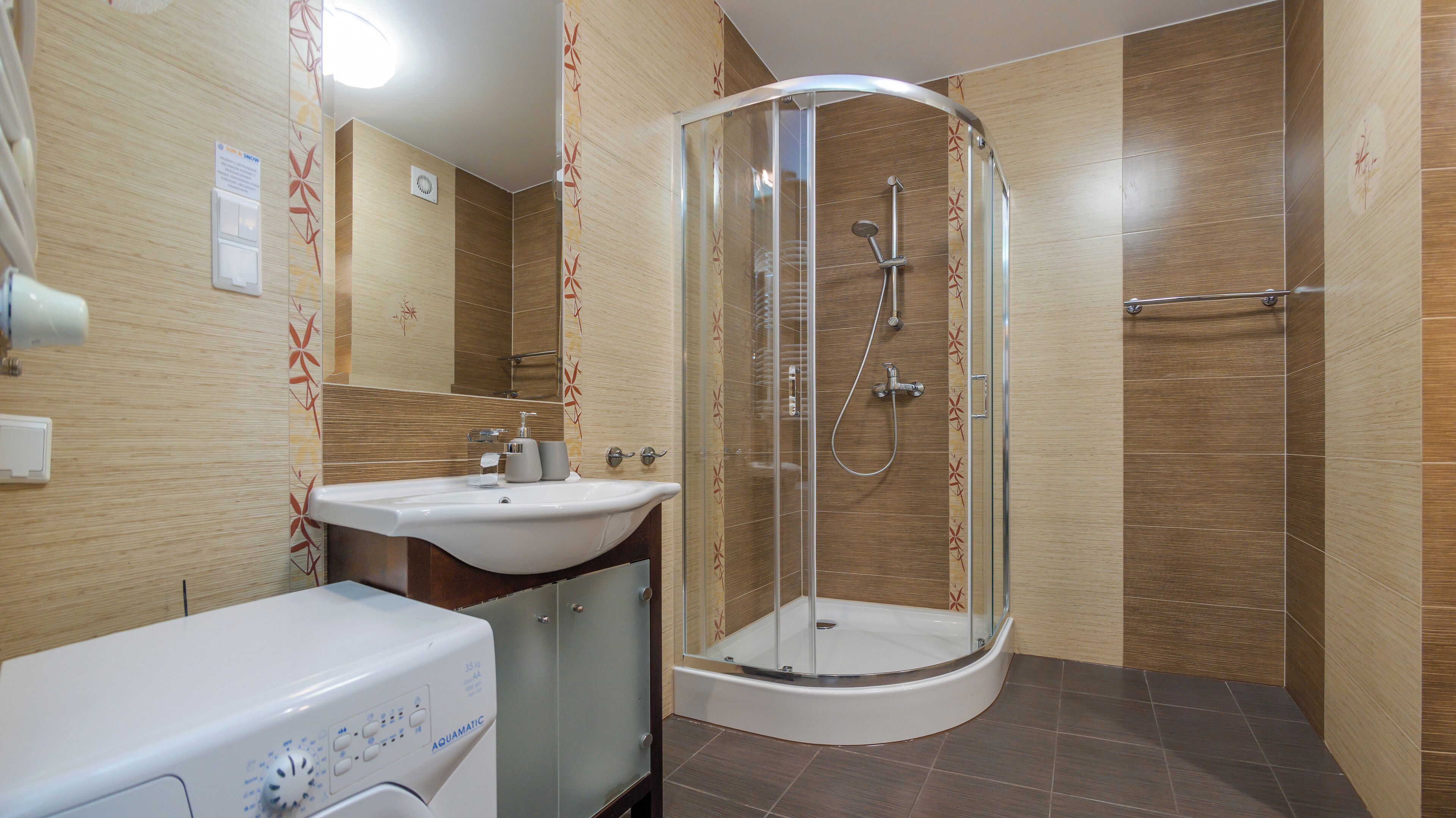 A modern bathroom with a glass-enclosed shower, a sink, and a washing machine.