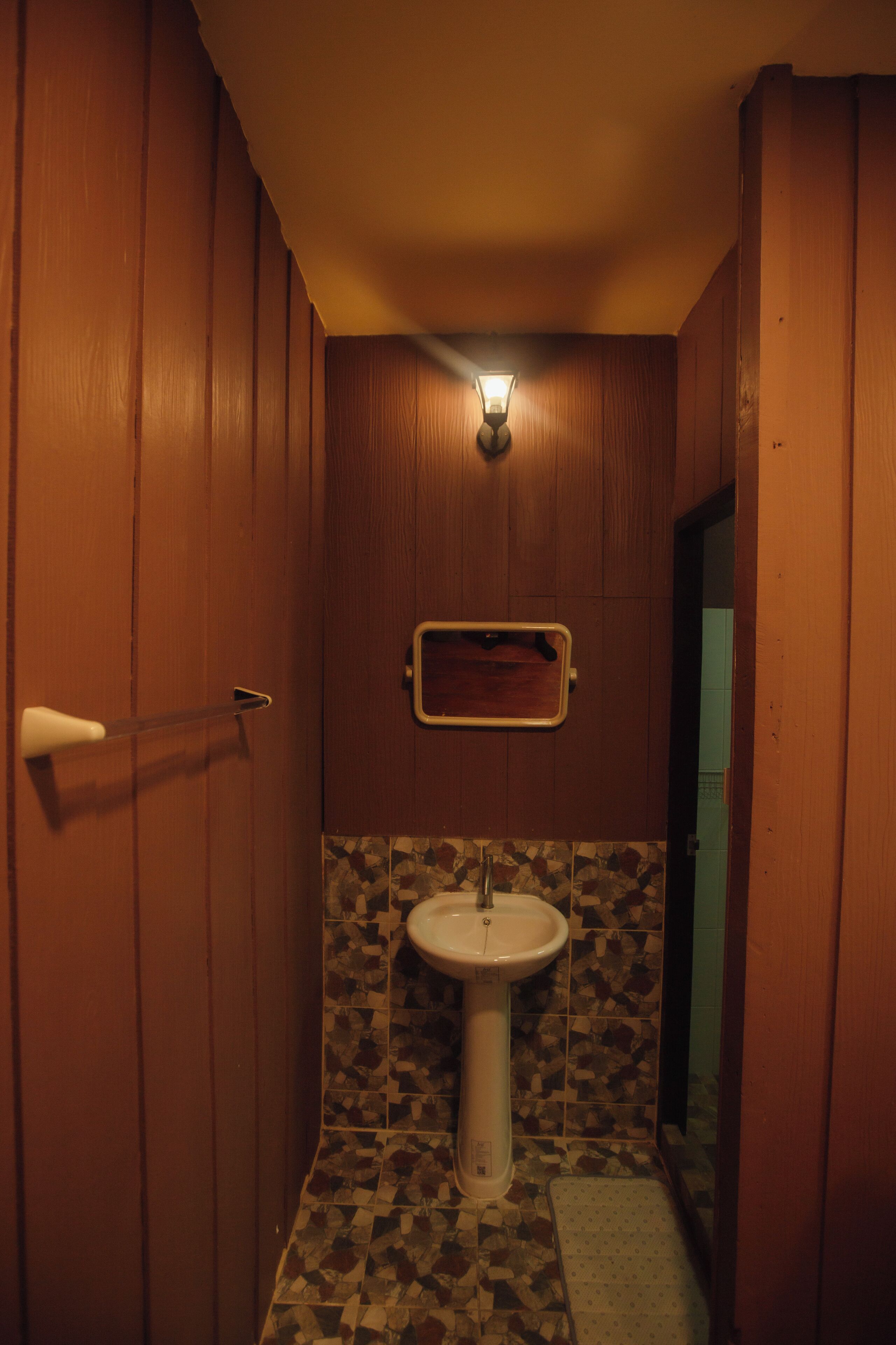 A small bathroom with a wooden door, a white sink, and a mosaic tile backsplash.