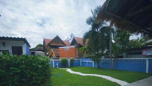 A residential backyard with a well-maintained lawn, a white gravel path, and a blue fence. - Agga CNX Hostel (Chiang Mai)