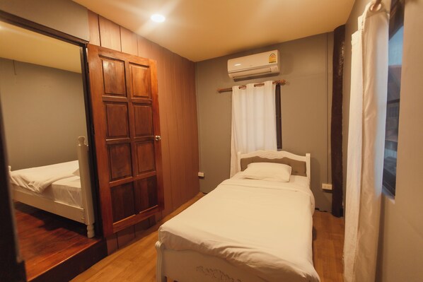 A bedroom with a wooden wardrobe, a single bed, and an air conditioning unit mounted on the wall. - Agga CNX Hostel (Chiang Mai)