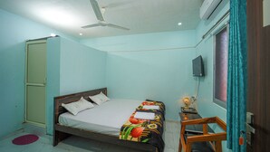 Une chambre à coucher avec un lit, un ventilateur de plafond, un climatiseur, une télévision, une petite table avec une lampe et une chaise en bois.