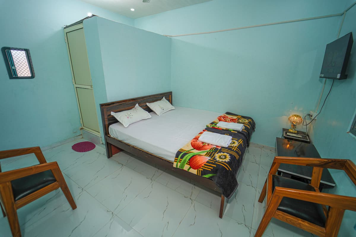 A single bed with a floral bedspread, a bedside table with a lamp, and two wooden chairs.