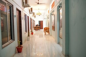 A hallway with a ceiling fan, potted plants, a dining table with chairs, and framed pictures on the walls. - Hotel Ramlalla palace (Faizabad)