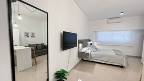 Un dormitorio moderno con cama, mesita de noche, televisor y una planta en maceta.