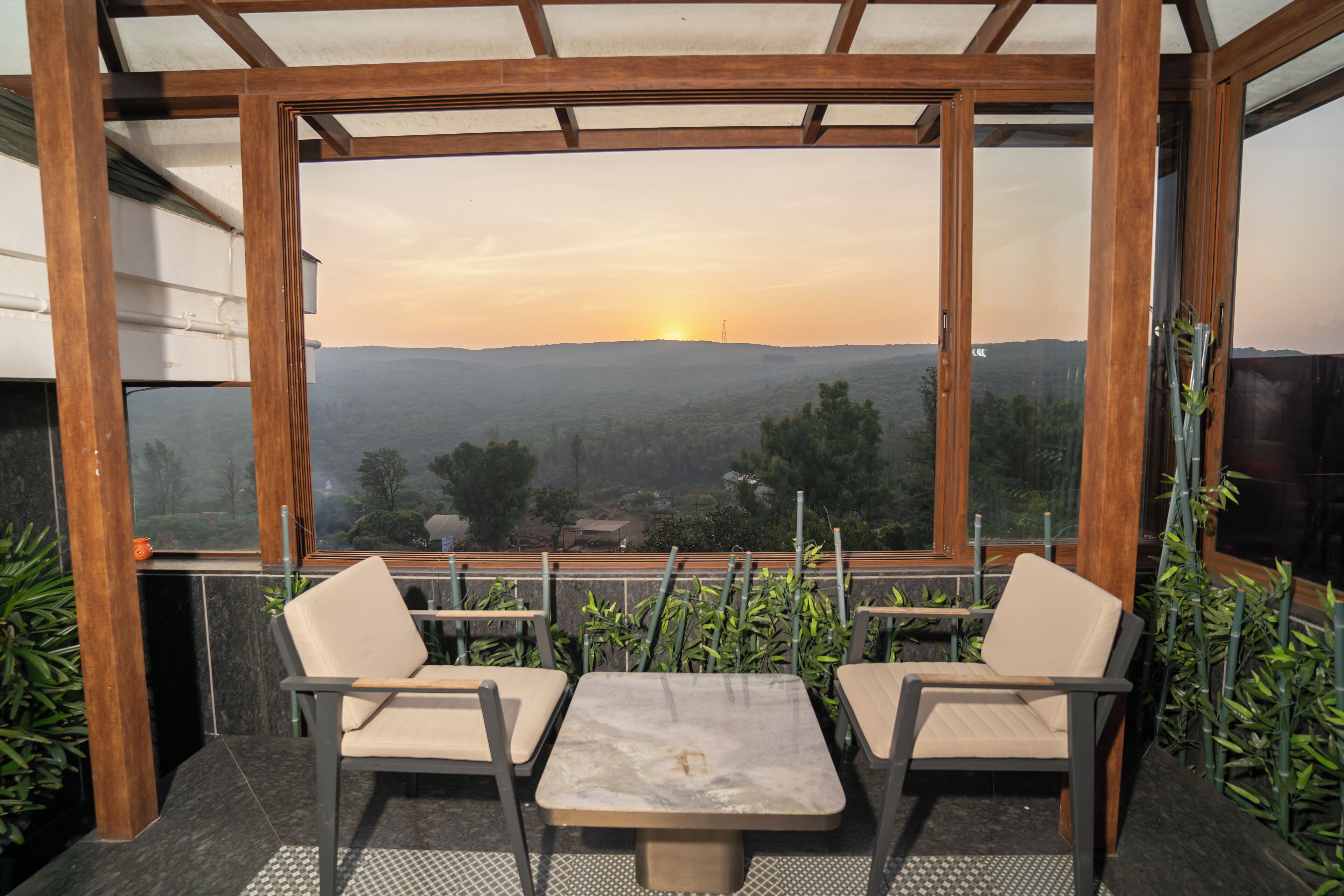 Una terraza con una mesa y dos sillas, con vistas a un paisaje pintoresco de colinas y un atardecer.