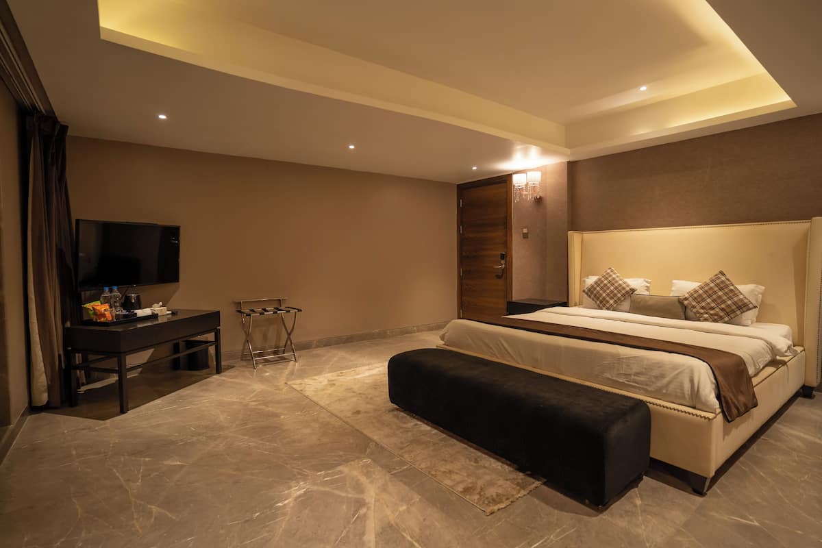 A modern bedroom with a large bed, a bedside table, a TV, and a bench.