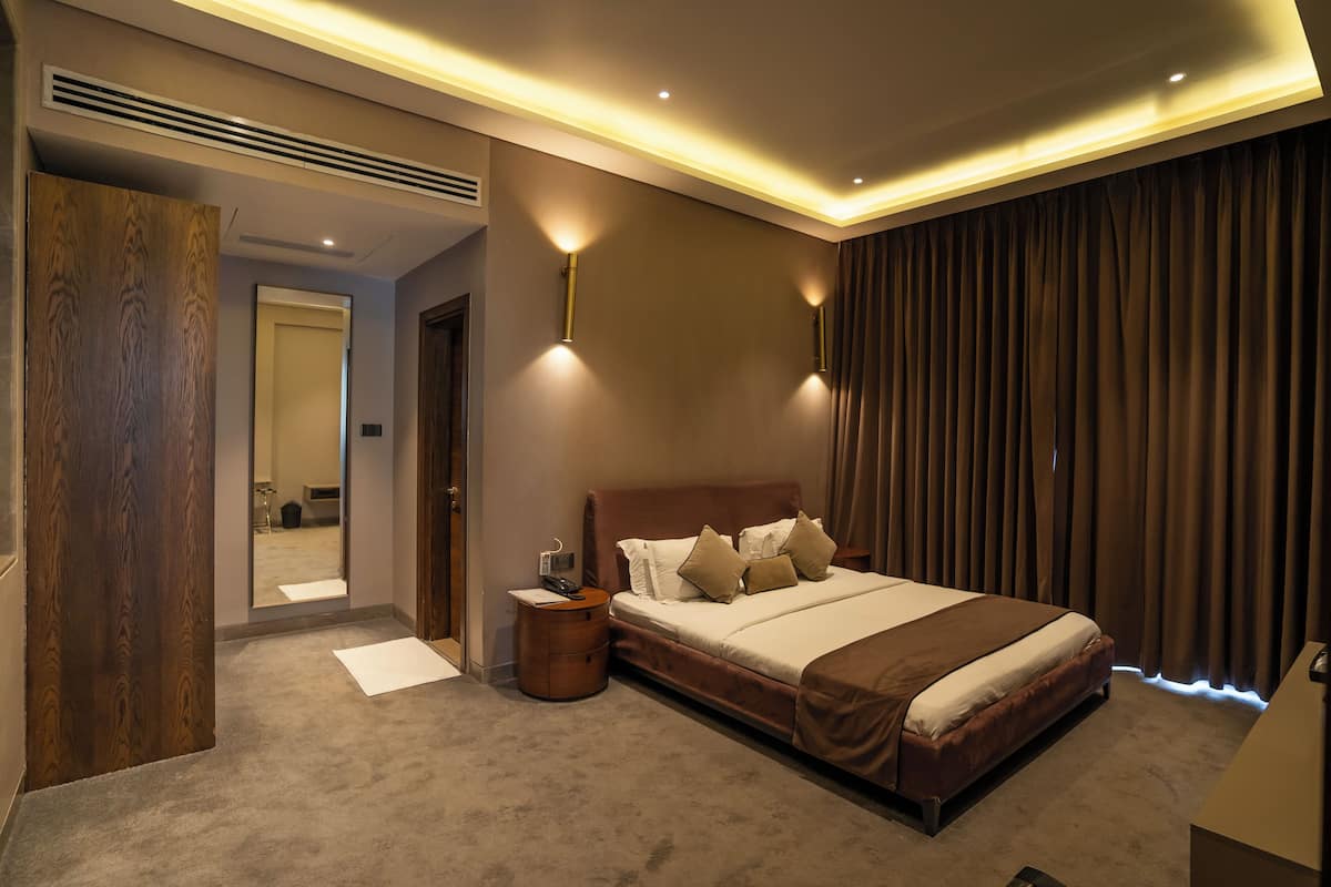A modern hotel room with a large bed, a bedside table, a mirror, and a wardrobe.