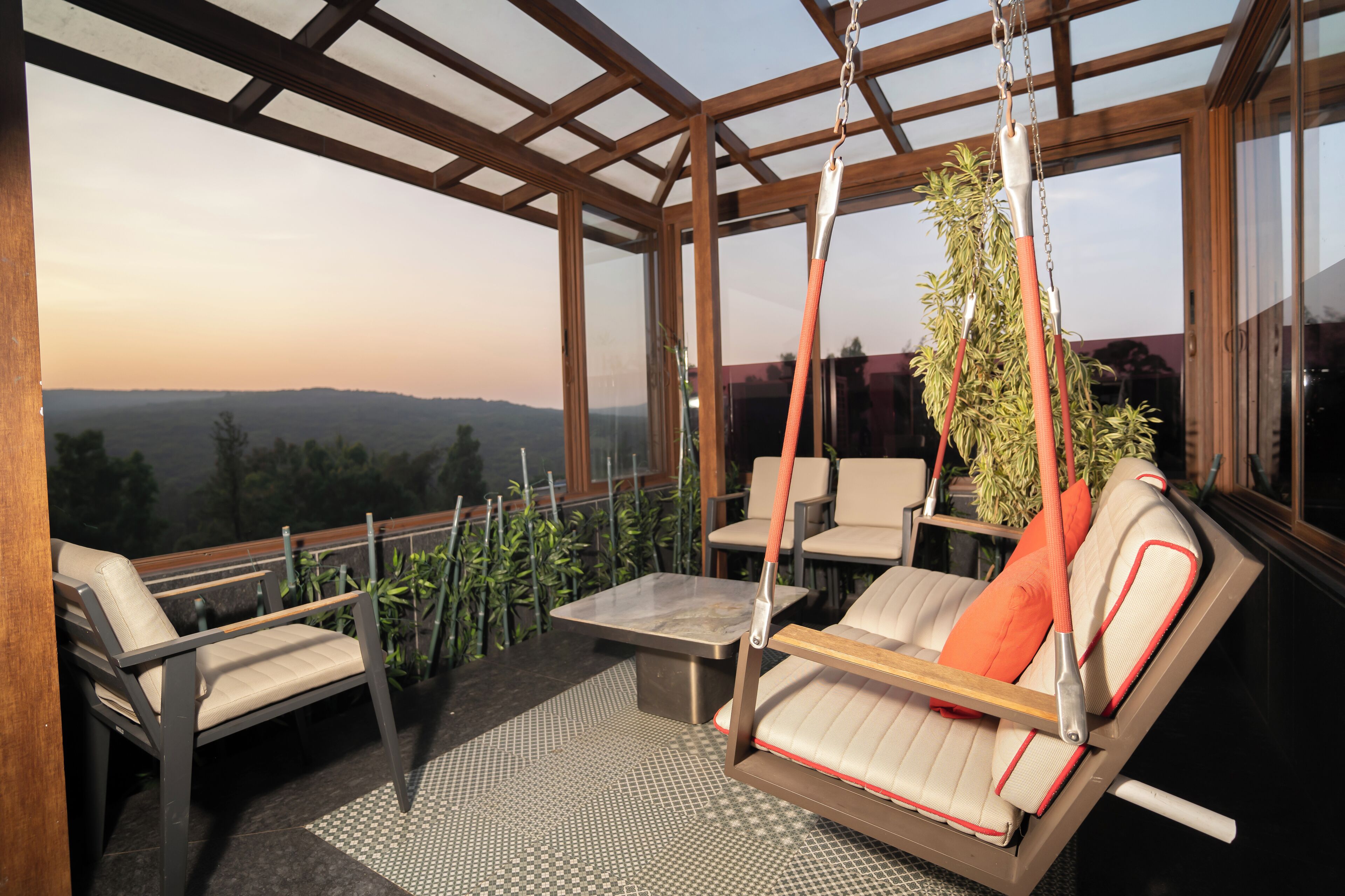 Zona de estar al aire libre iluminada por el sol con una silla colgante, una mesa y sillas, con vistas a un paisaje pintoresco.