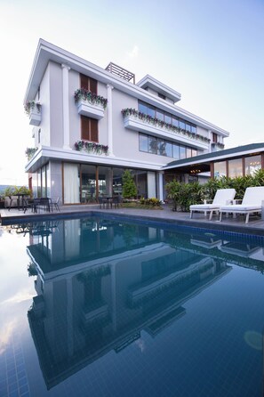 Ein modernes, zweistöckiges Haus mit Swimmingpool, Sitzgelegenheiten im Freien und einem Balkon mit Pflanzen.