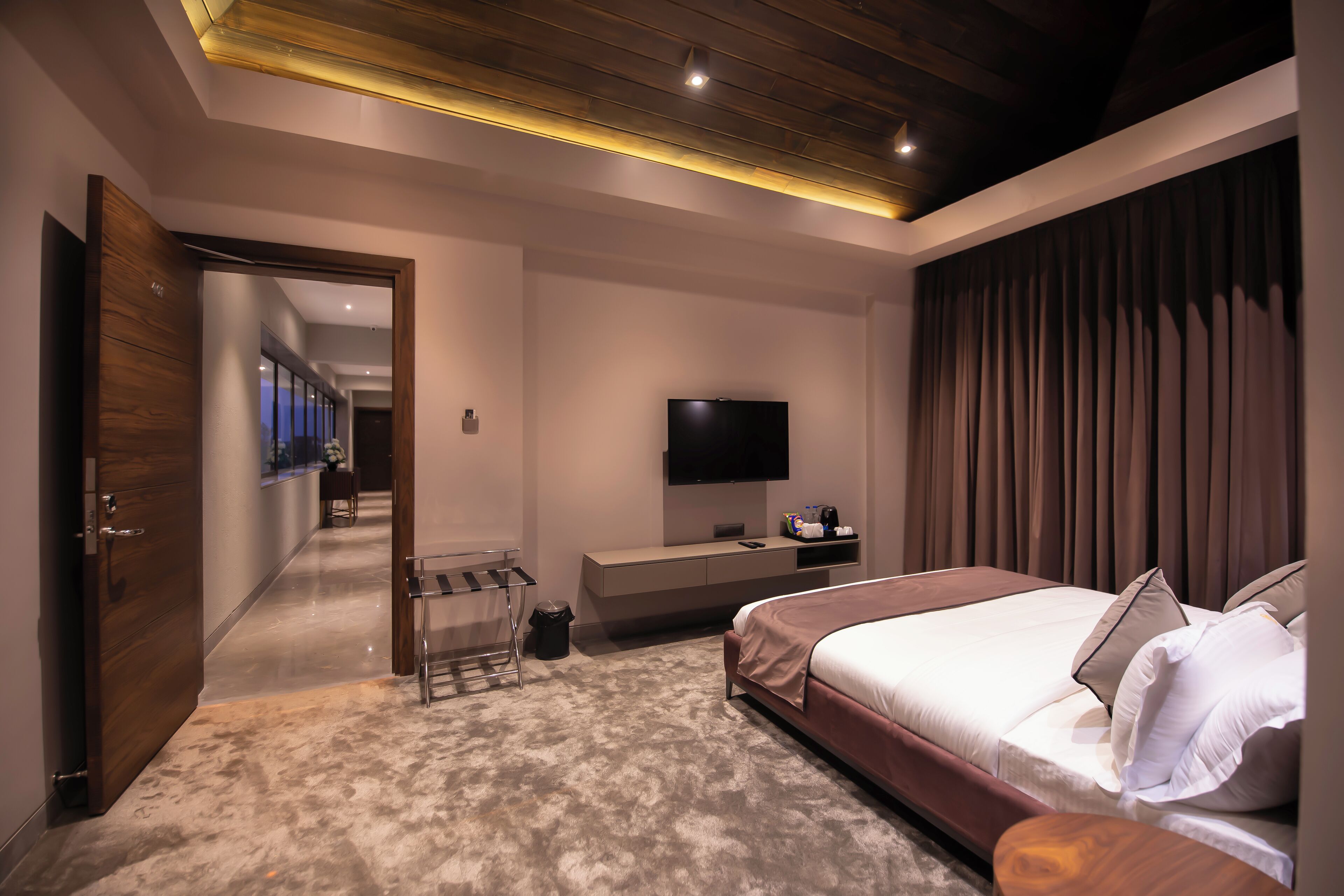 A modern bedroom with a large bed, a TV mounted on the wall, and a wooden door leading to another room.