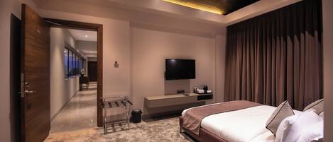 A modern bedroom with a large bed, a TV mounted on the wall, and a wooden door leading to another room.