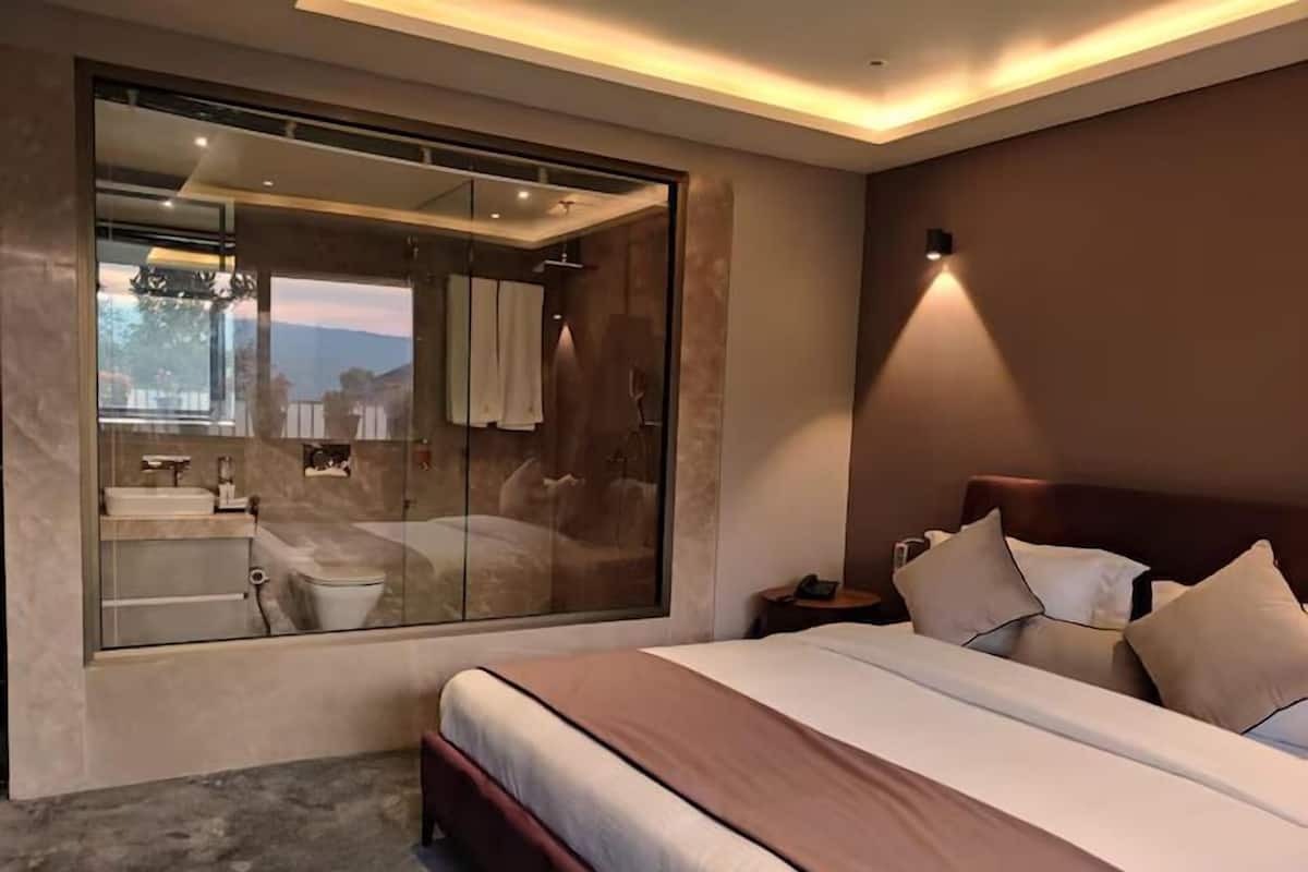 A modern bedroom with a large bed, a glass-enclosed bathroom, and a nightstand with a lamp.
