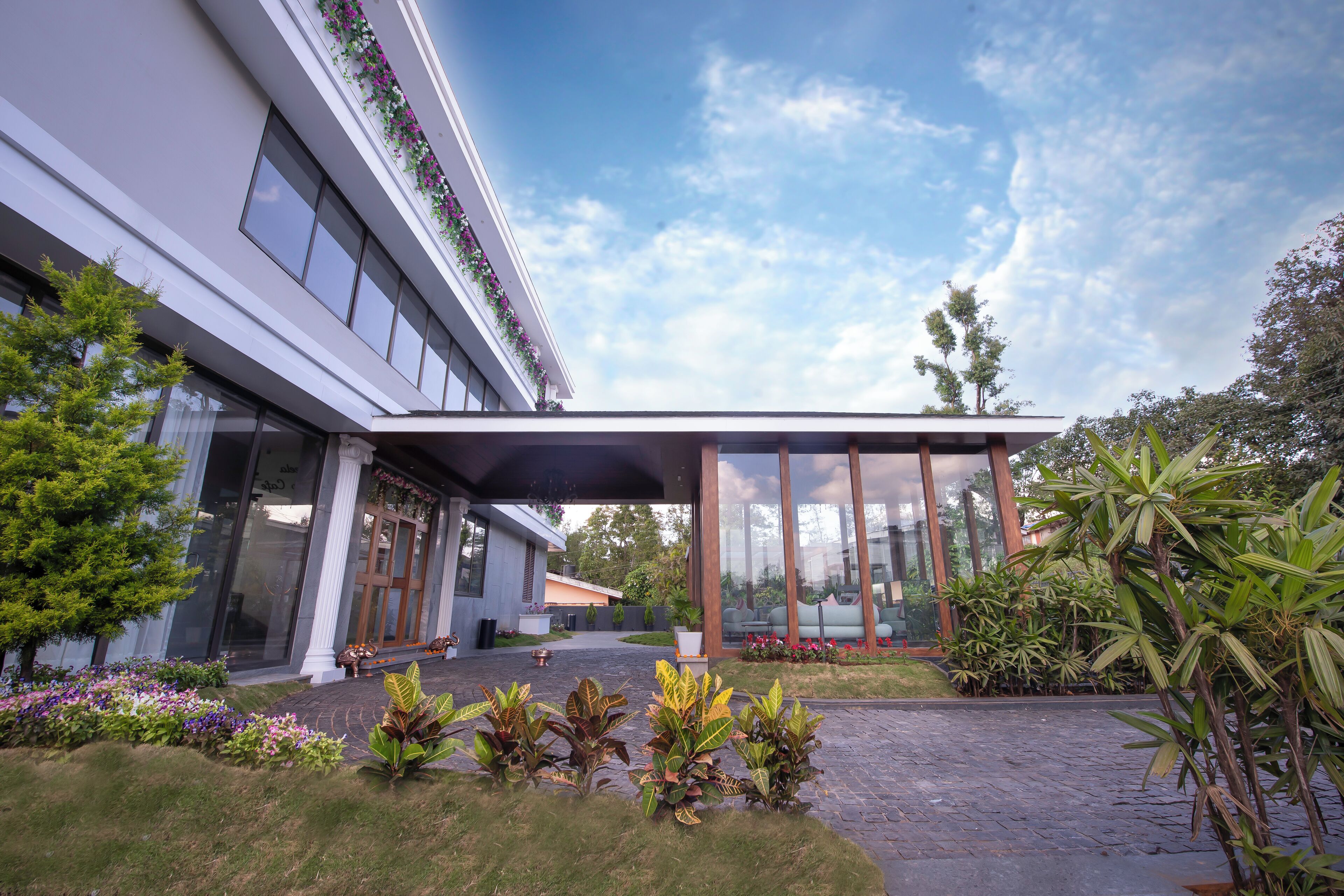 A modern building with large windows, a covered entrance, and a landscaped garden with various plants.