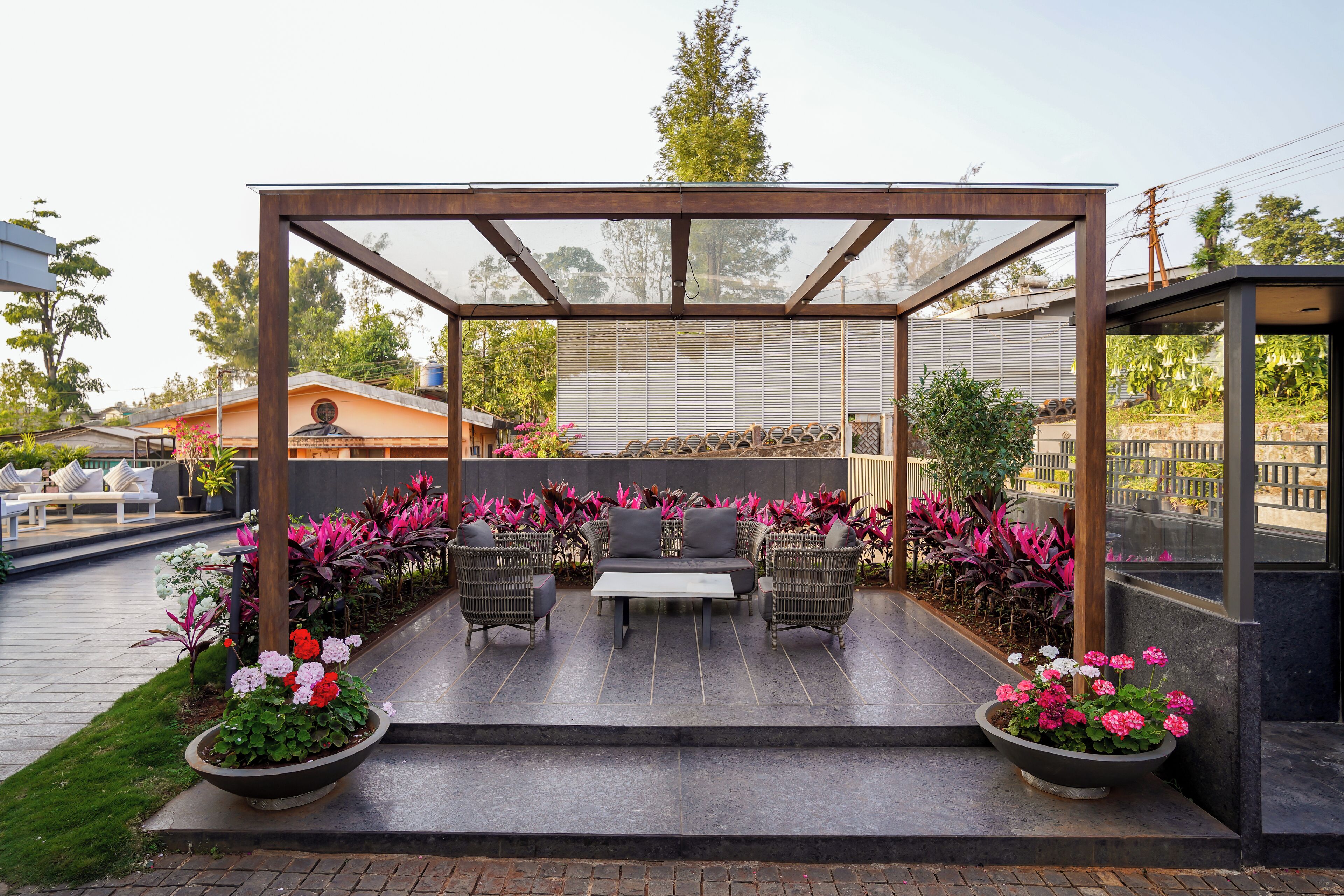 Eine Terrassengruppe im Freien mit überdachtem Sitzbereich, umgeben von Blumentöpfen und Blumen.