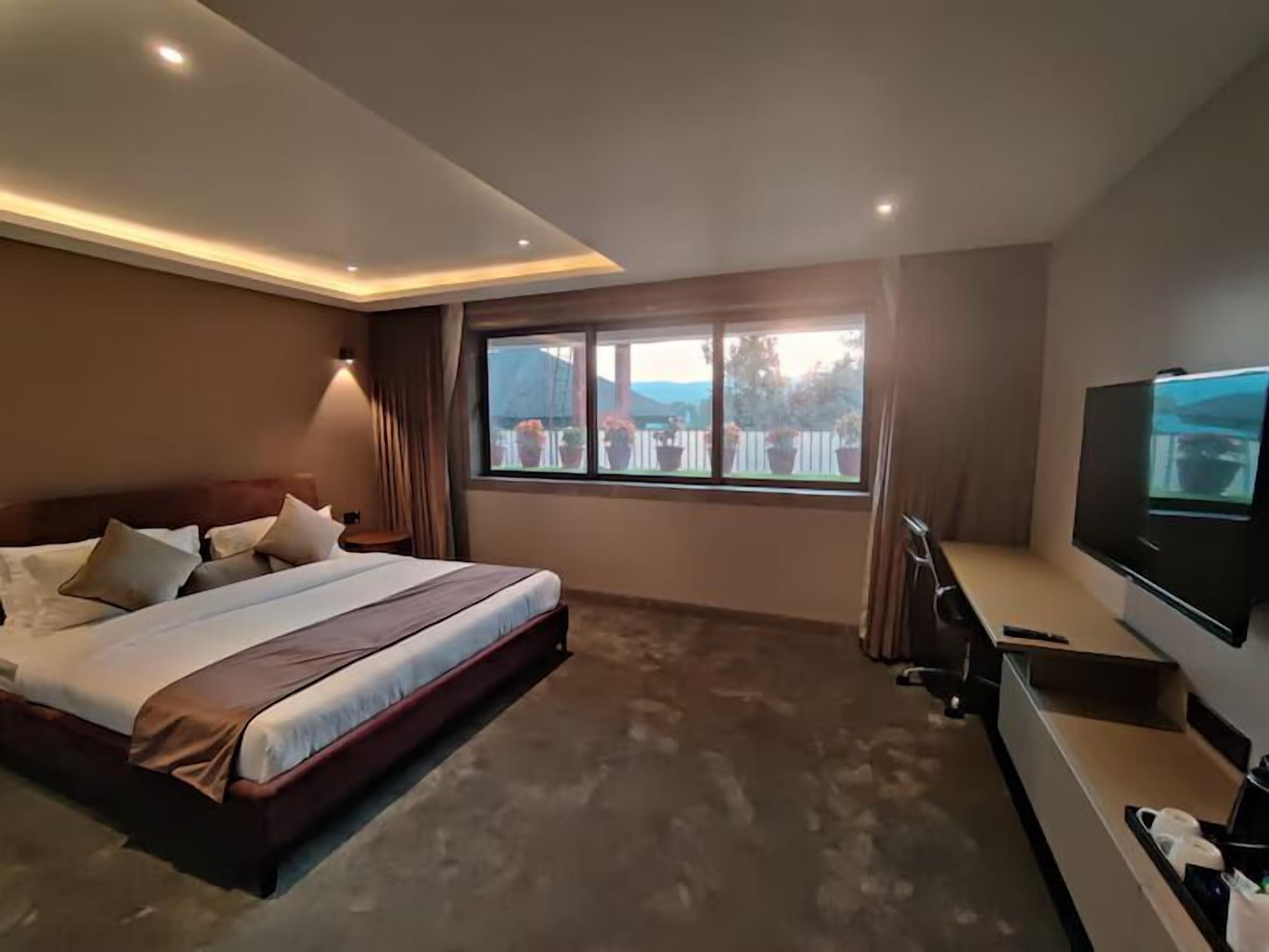 A hotel room with a large bed, a TV, and a view of the outdoors.
