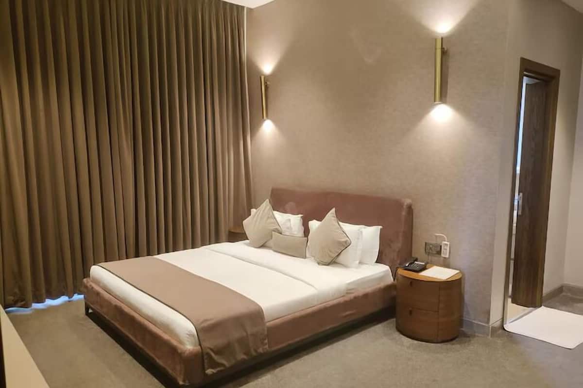 A hotel room with a large bed, a bedside table, a lamp, and a curtain.