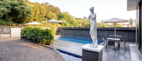 Piscina com estátua, área de estar externa e caminho de tijolos.