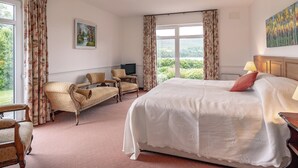 Hotelkamer met een groot bed, twee fauteuils, een bank, een televisie en een schilderij aan de muur.