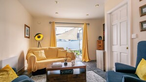 Ein gemütliches Wohnzimmer mit einer Couch, zwei Sesseln, einem Couchtisch und Blick durch eine Tür nach draußen.