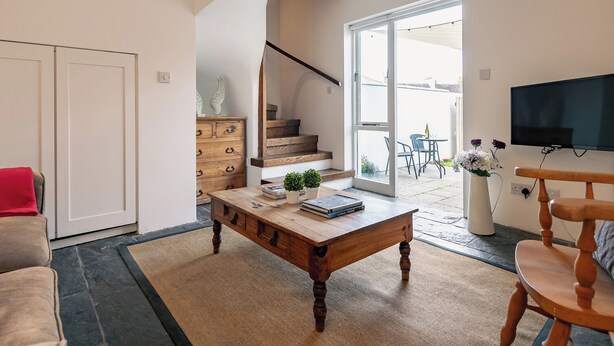 Una sala de estar moderna con una mesa de centro de madera, un televisor montado en la pared y una escalera que lleva a un patio exterior.