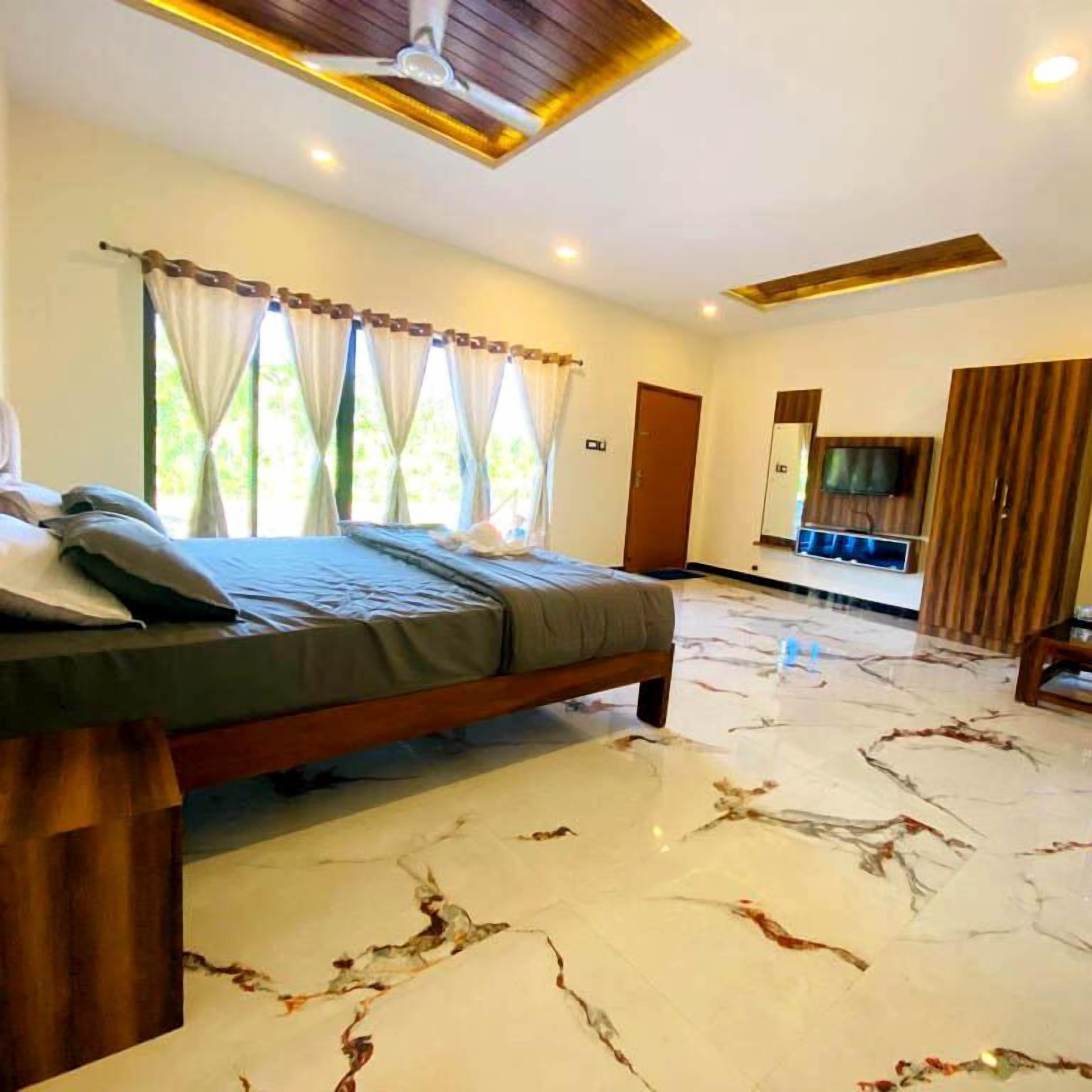 A bedroom with a bed, curtains, a ceiling fan, and a TV in the adjacent room.