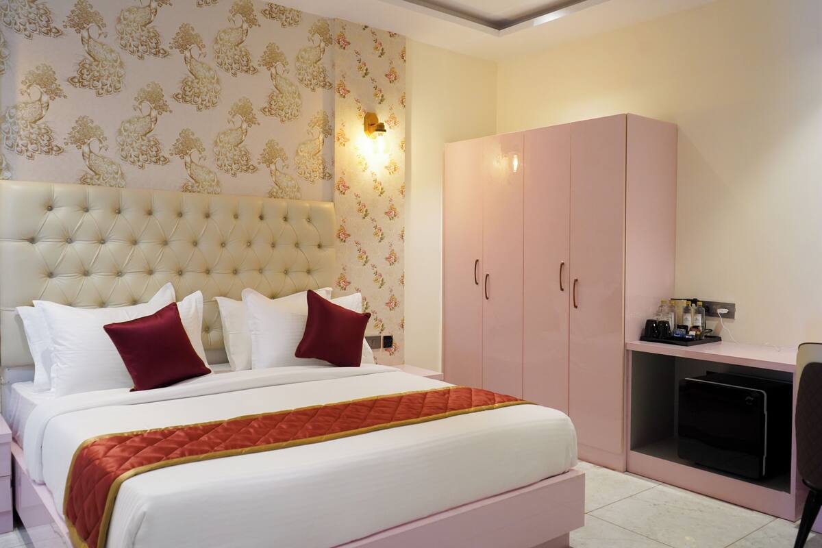 A bedroom with a tufted headboard, a bed with white and red bedding, a pink wardrobe, and a desk with a chair.