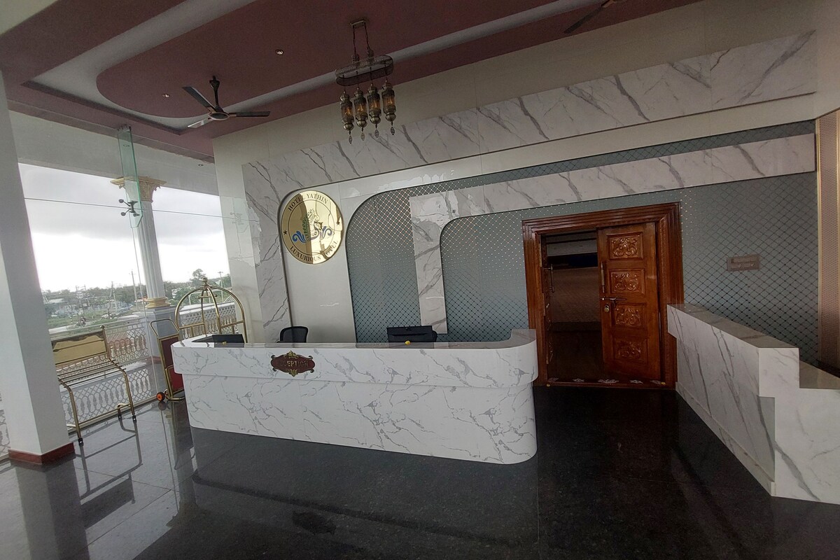 A hotel reception area with a marble counter, a chandelier, and a view of the city through large windows.