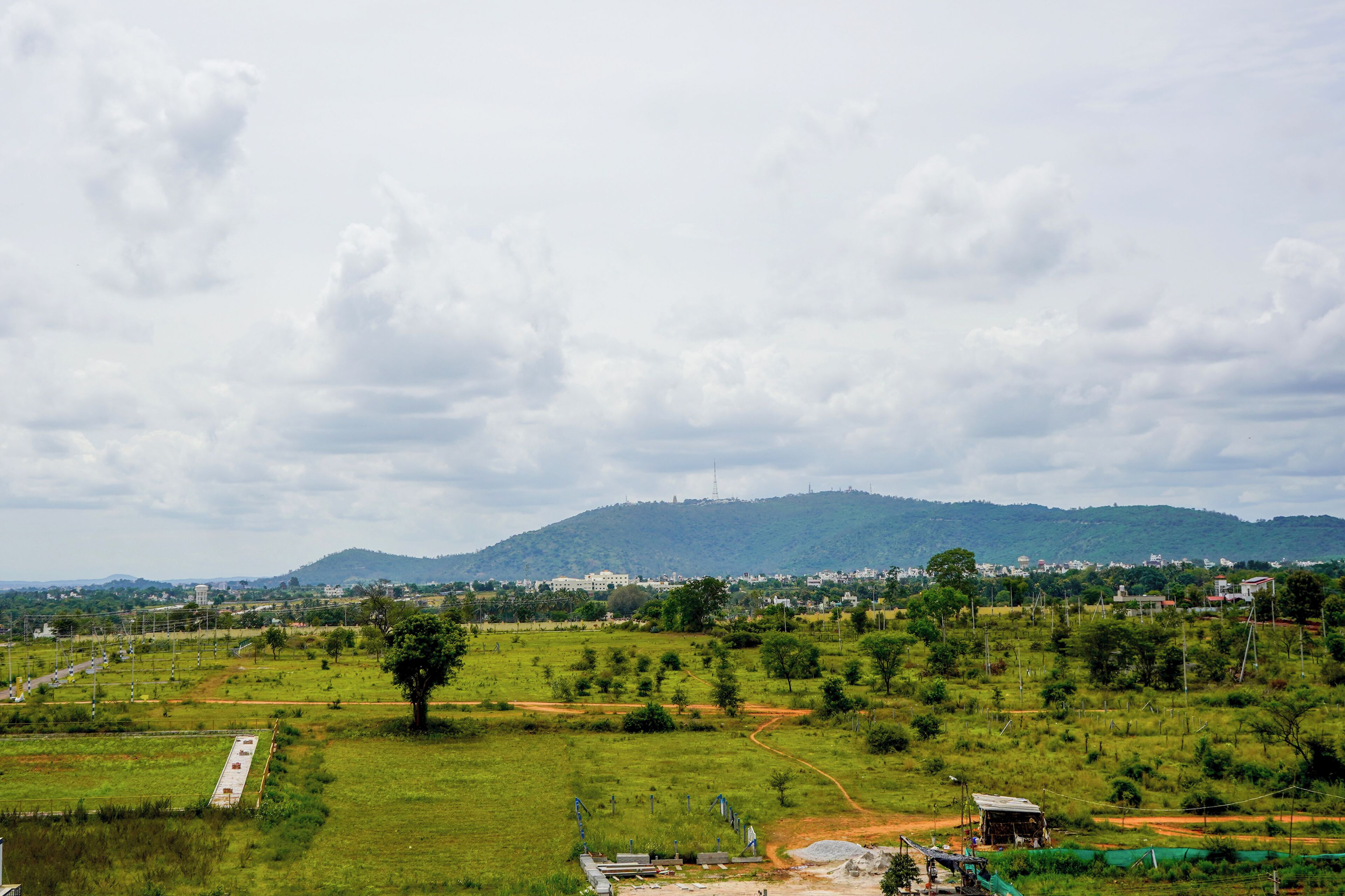 A rural landscape with a dirt road, green fields, and a distant hill with buildings.