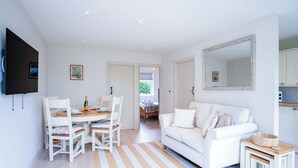 A modern, white-themed living room with a dining area, a sofa, and a small kitchen area. - Bayview 3 - 2 Bedroom - Bayview Oxwich (Swansea)