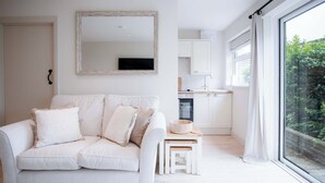 A modern, minimalist living room with a white sofa, a small wooden table, and a large window offering a view of greenery. - Bayview 3 - 2 Bedroom - Bayview Oxwich (Swansea)