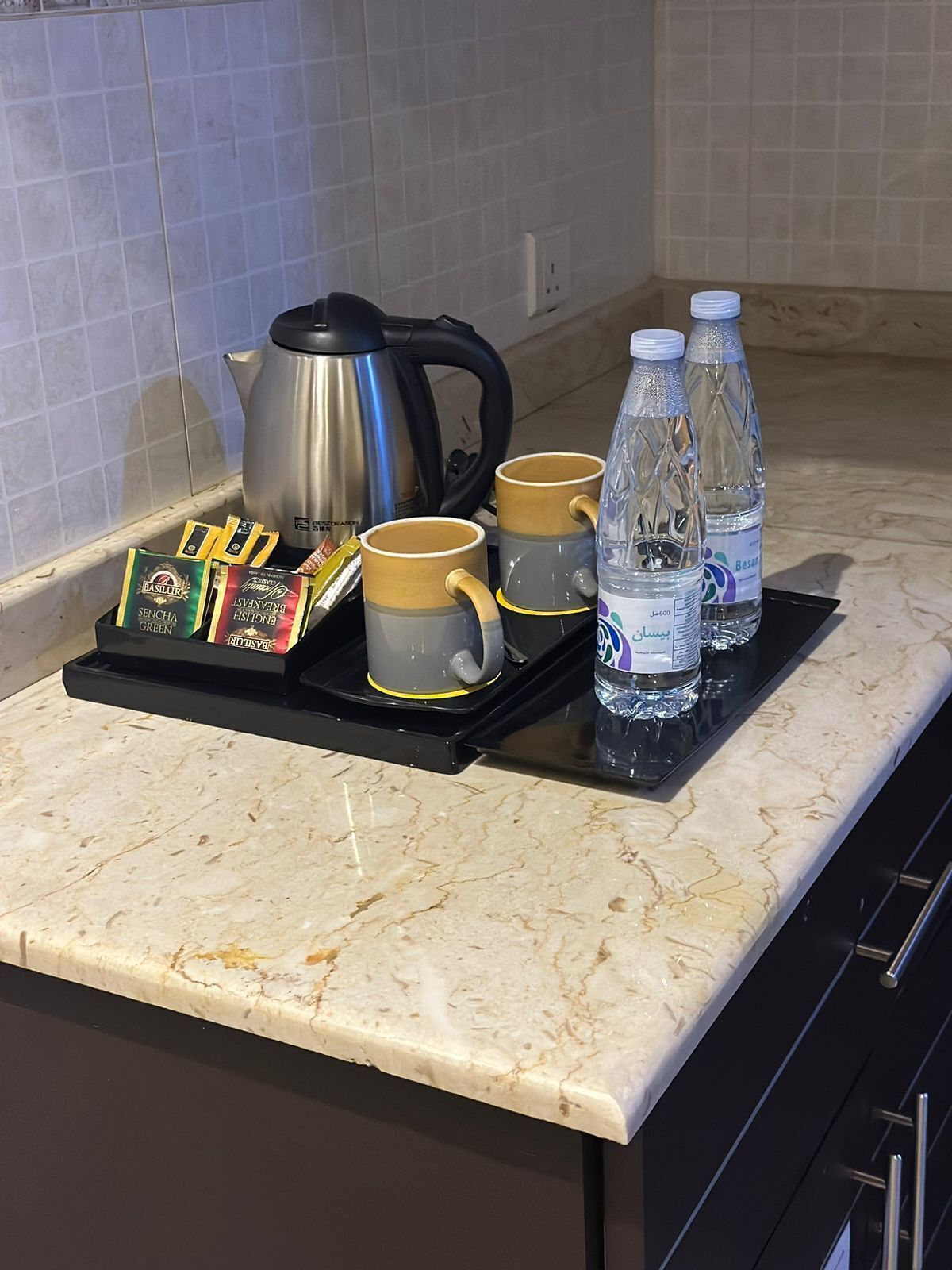 Una encimera de cocina con una cafetera, cuatro tazas, una bandeja con cápsulas de café y dos botellas de agua.