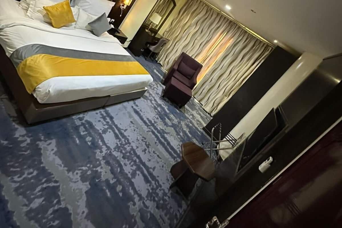A modern hotel room with a large bed, a desk, a chair, and a mirror.