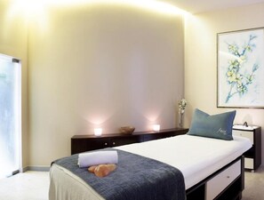 A bedroom with a bed, bedside tables, a nightstand, a wall-mounted lamp, and a framed artwork.