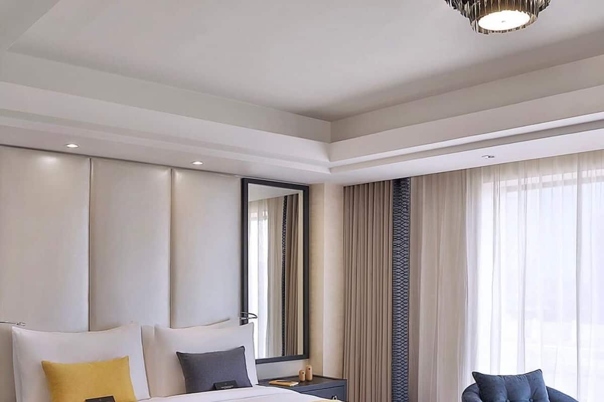 A hotel room with a large bed, two bedside tables, a chair, and a large window with curtains.