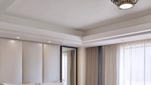 Habitación de hotel con una cama grande, dos mesitas de noche, una silla y un ventanal con cortinas.