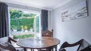A round wooden table with a compass design, surrounded by dark wooden chairs, in a room with a large window and a painting on the wall. - Bryn View – 5 Bedroom Holiday Home – Oxwich (Swansea)