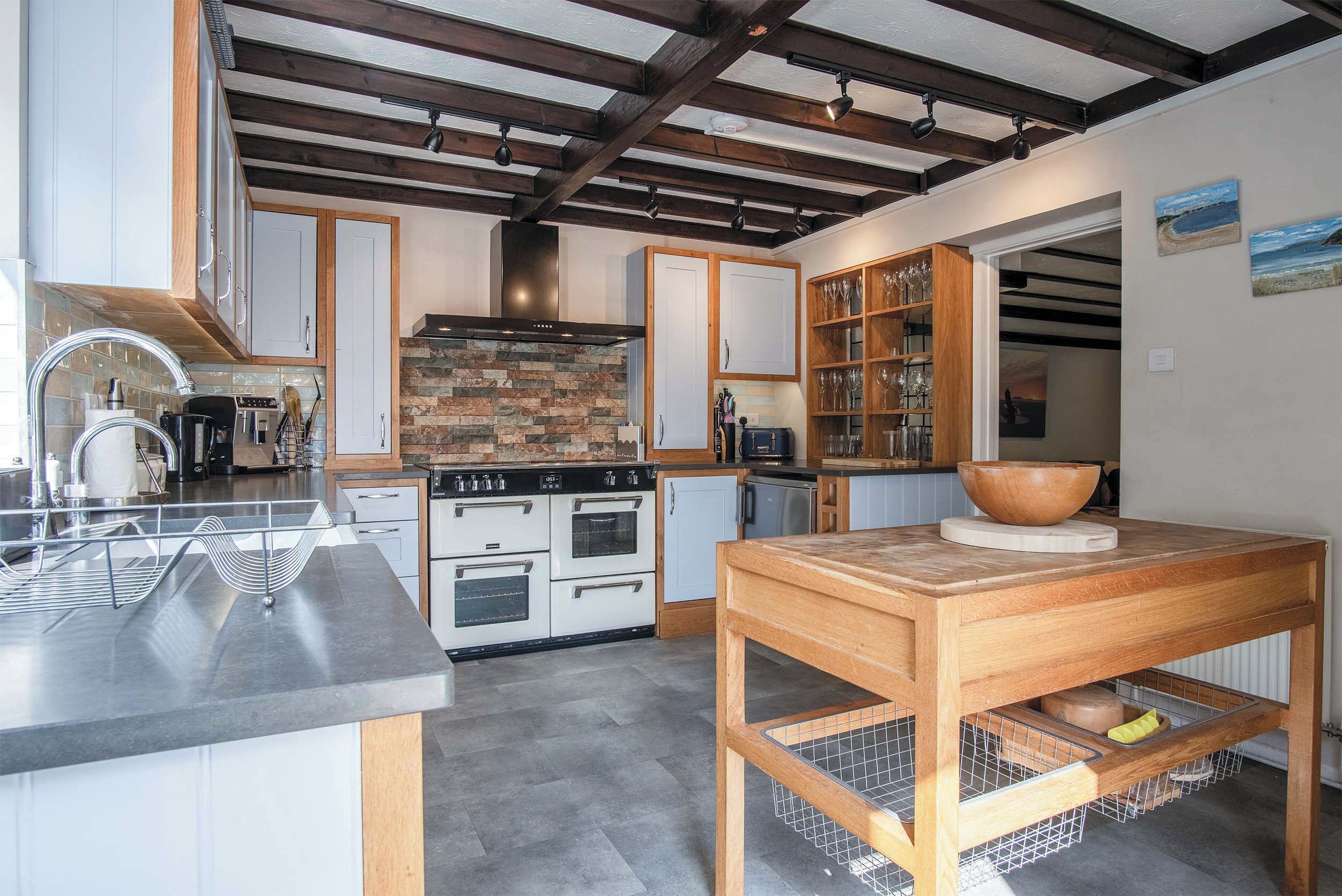 A modern kitchen with white cabinets, a wooden table, and a stone backsplash.