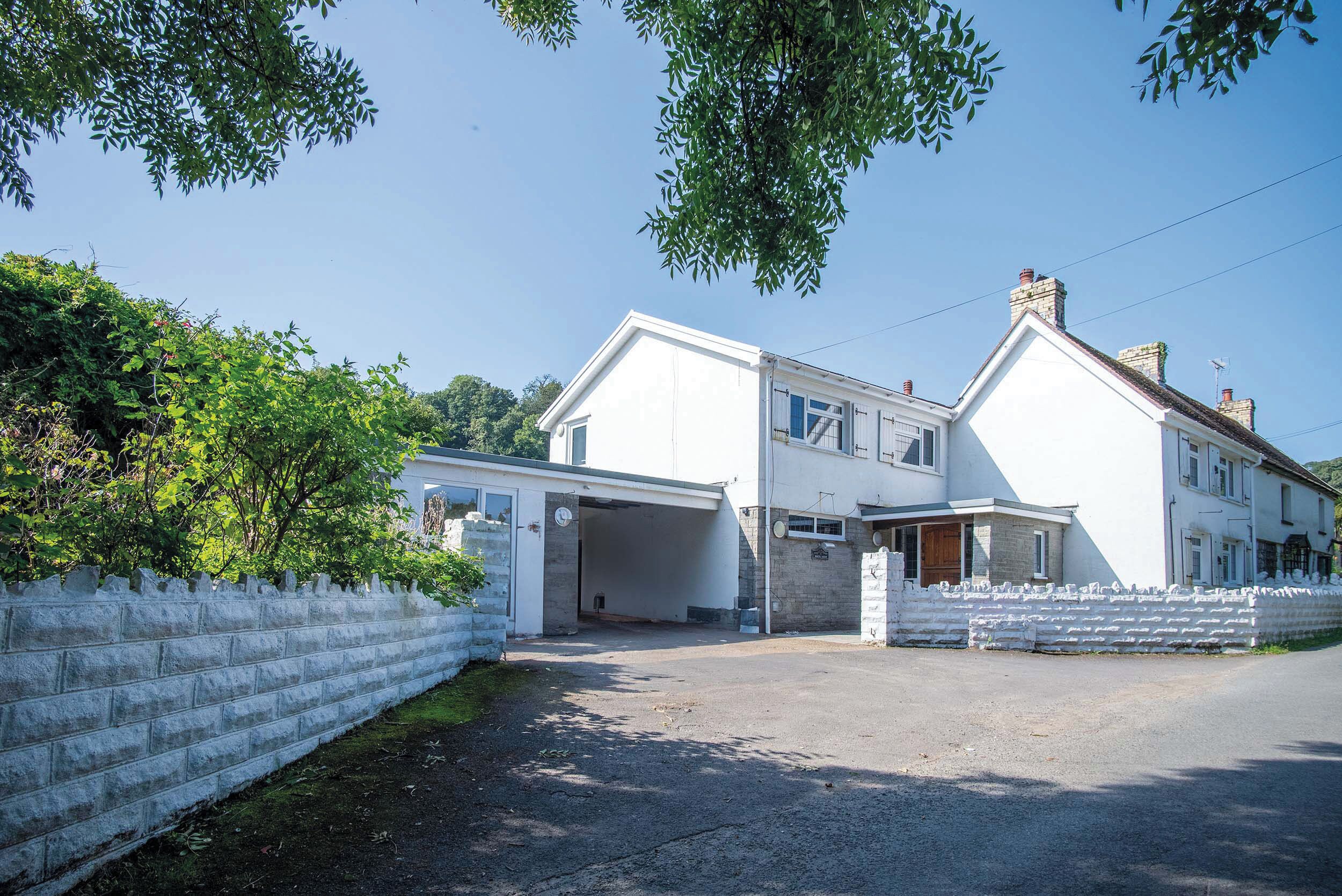 A two-story house with a garage, surrounded by a white fence and greenery.