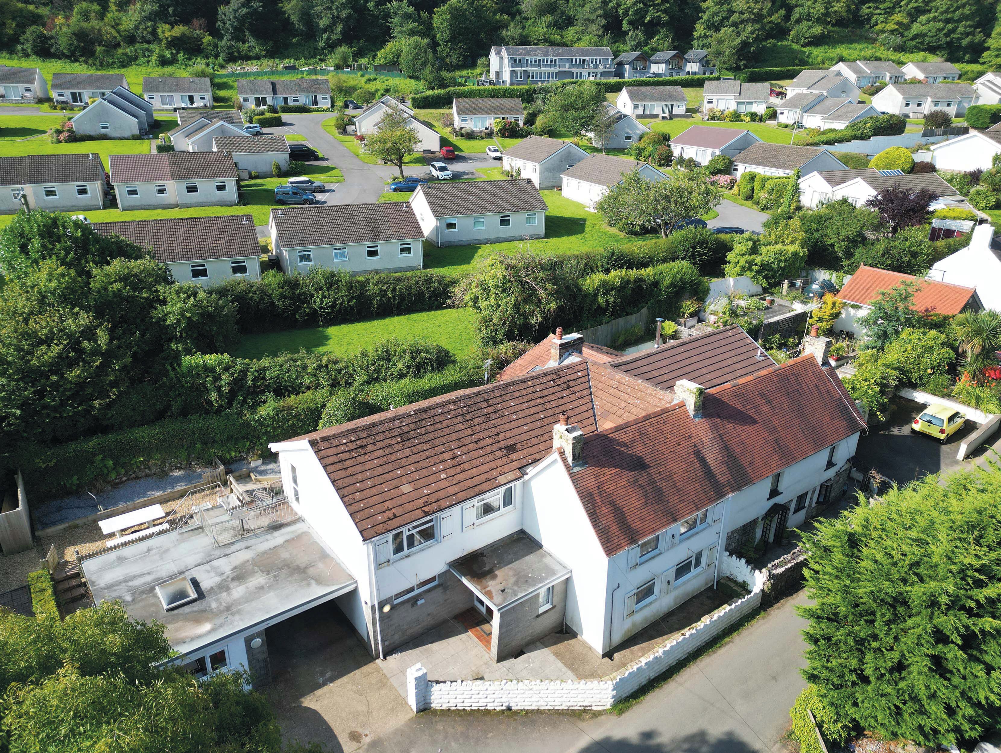 A residential area with multiple houses, a central white building with a red roof, and surrounding greenery.